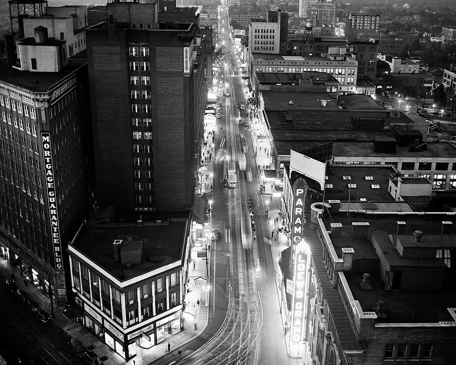1930s 1940s looking down city street pedestrians trolley cars neon signs at night from the Candler Photograph by Panoramic Images