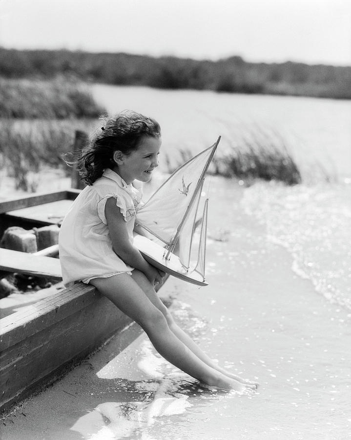 1930s Young Girl At Seashore Holding Sailboat Toy Sitting On Edge Of Rowboat Feet In Water Photograph by Panoramic Images 1930s Young Girl At Seashore Holding Sailboat Toy Sitting On Edge Of Rowboat Feet In Water Photograph by Panoramic Images