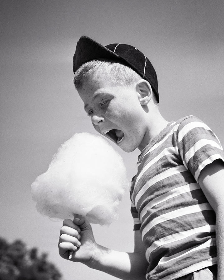 1950s Boy Wearing Baseball Cap And Striped Tee Shirt Mouth Wide Open Eating Carnival Cotton Candy Photograph by Panoramic Images