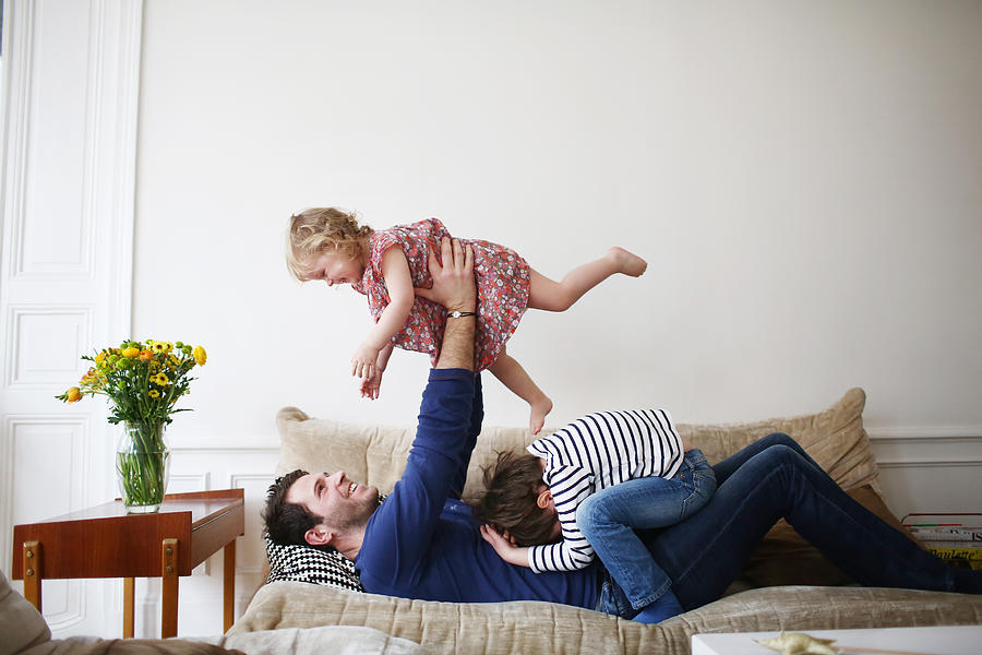 A dad playing with his children on a sofa #2 Photograph by Catherine Delahaye