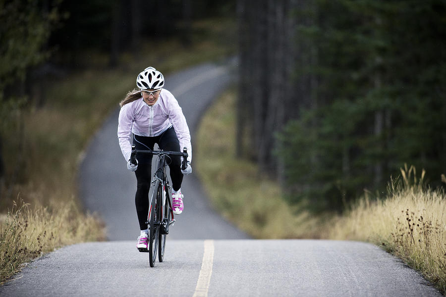 A woman rides her road bike along the Trans Canada Trail bikepath near Canmore, Alberta, Canada in the autumn. #2 Photograph by GibsonPictures