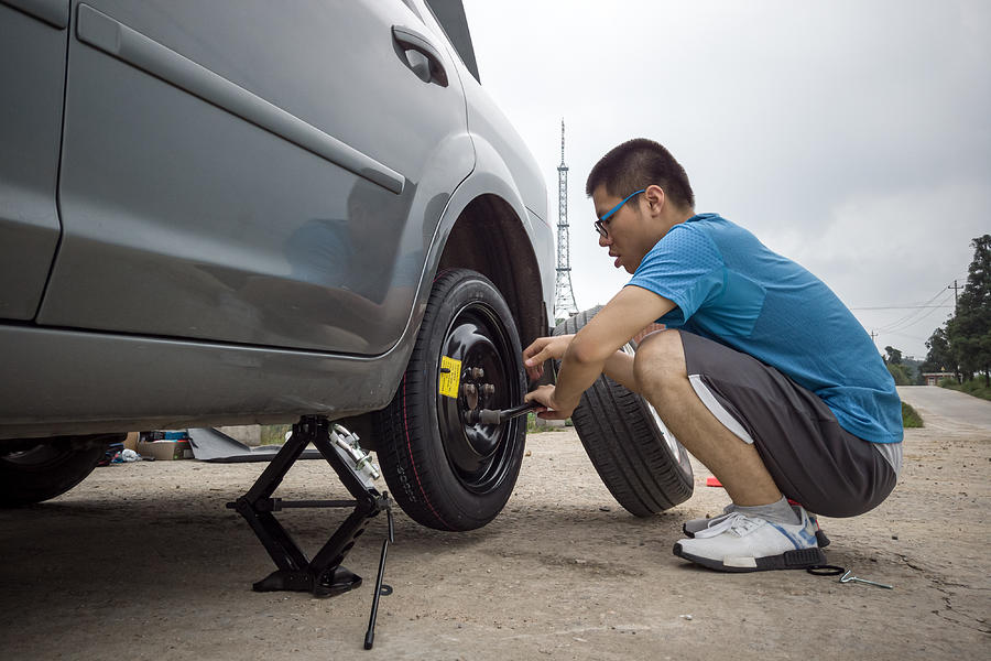 A young man changing a tire on the side of the road #2 Photograph by Zhihao