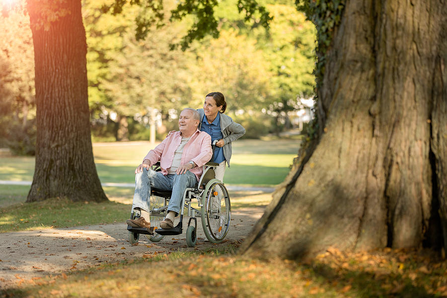 Caregiver and senior man on a wheelchair walking outdoors #2 Photograph by FredFroese