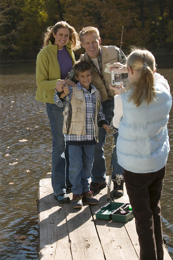Girl taking photograph of family fishing #2 Photograph by Comstock Images