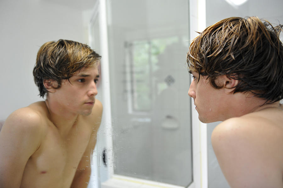 One teenage boy checking his face in the bathroom mirror #2 Photograph by Lighthousebay