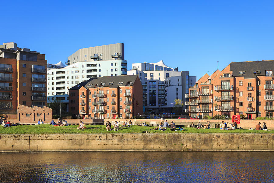 People enjoying the sunshine near apartments by the river Aire in Leeds, Yorkshire. #2 Photograph by Kelvinjay