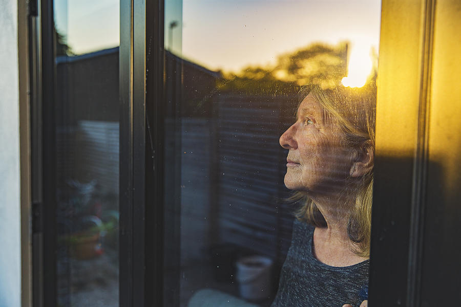 Senior woman looking through window #2 Photograph by Justin Paget