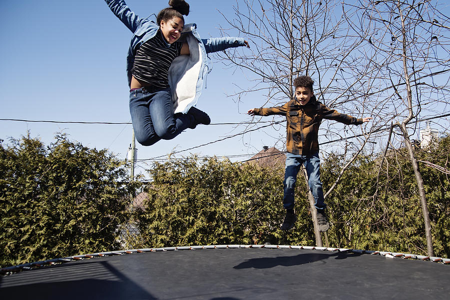 Siblings jumping on trampoline outdoors in springtime. #2 Photograph by Martinedoucet