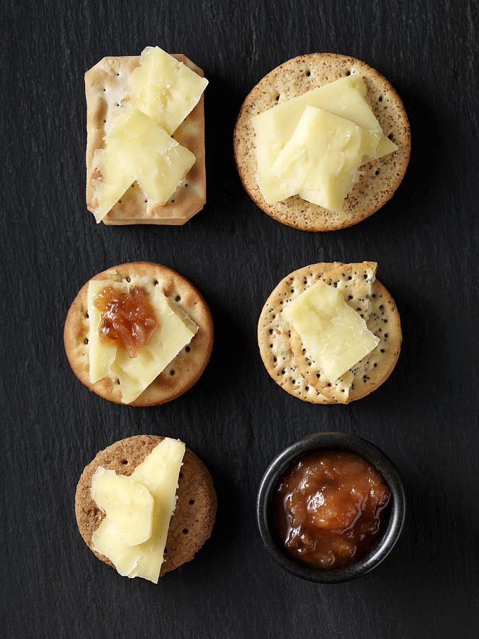 Still life of variety of cheese crackers with cheddar cheese and chutney on black slate, overhead view #2 Photograph by Danielle Wood