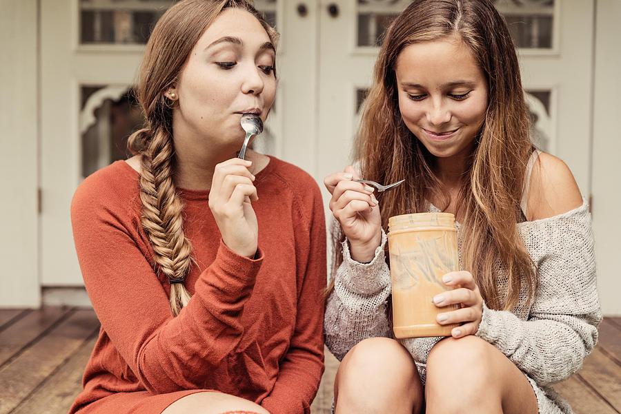 Teenage girlfriends eating peanut butter by the spoon on porch. #2 Photograph by Martinedoucet