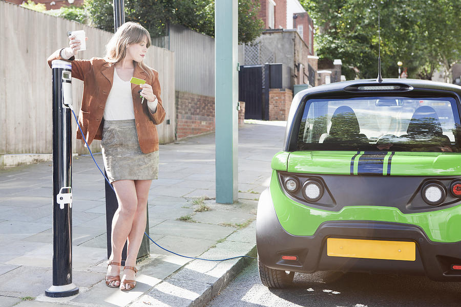 Woman charging electric car on street #2 Photograph by Nancy Honey
