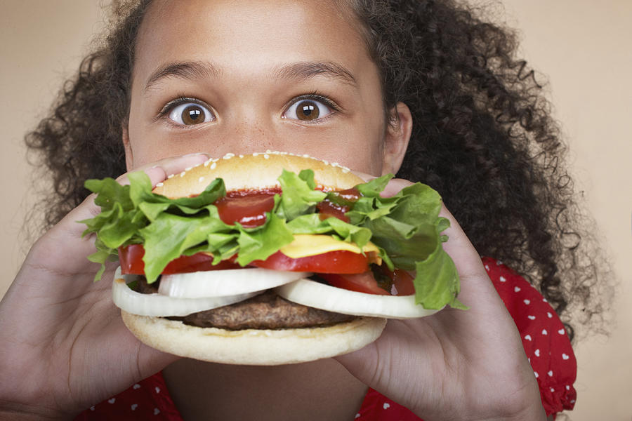 Young girl indoors eating a hamburger #2 Photograph by Tom Merton