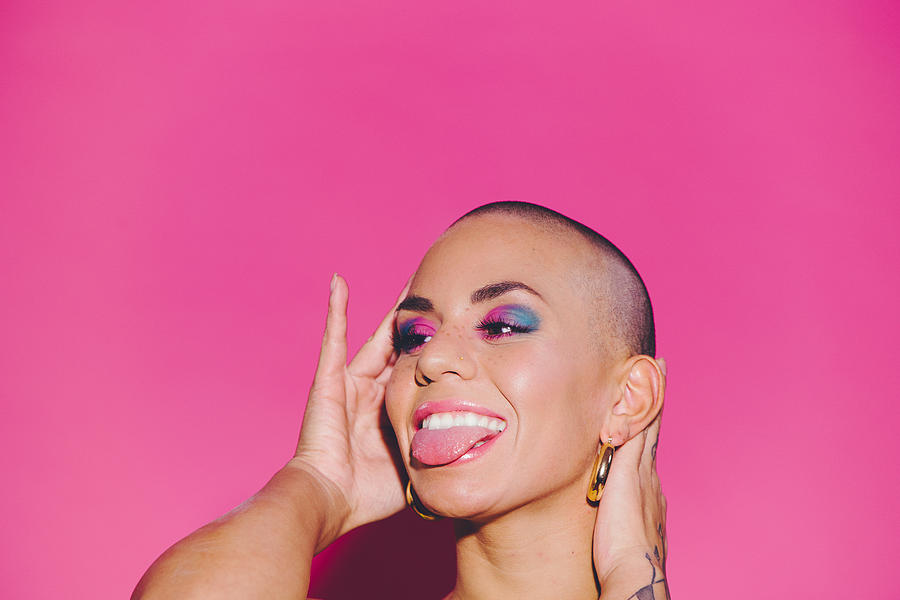 Young happy beautiful woman against a pink background sticking out her tongue. #2 Photograph by Hugo Goudswaard