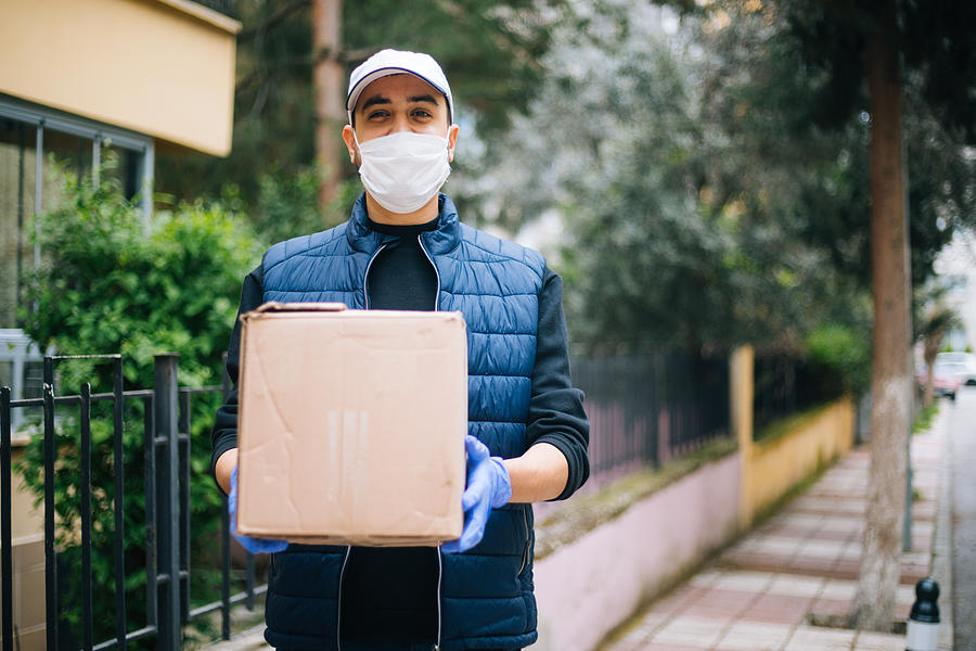 Young happy delivery man with protective mask looking at camera #2 Photograph by Agrobacter