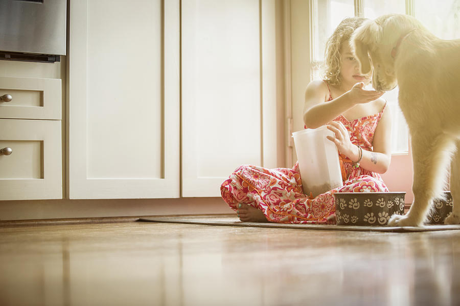 Caucasian girl sitting on kitchen floor feeding dog #3 Photograph by Terry Vine