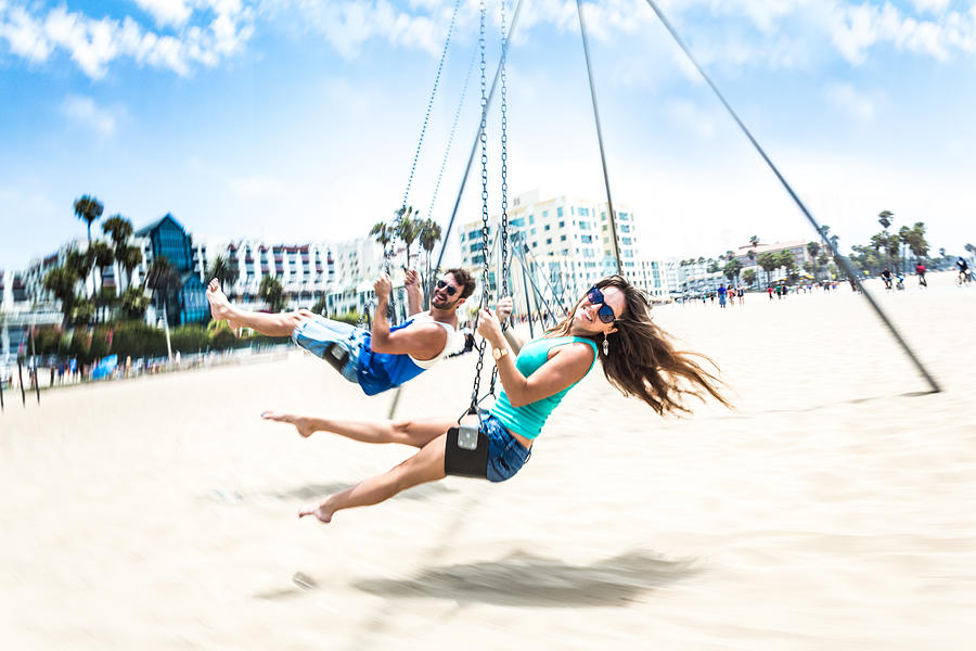 Couple teetering on swings LA beach #3 Photograph by Itsskin