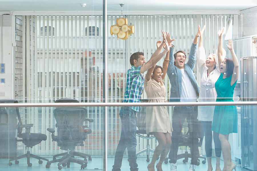 Excited business people with arms raised at window #3 Photograph by Martin Barraud
