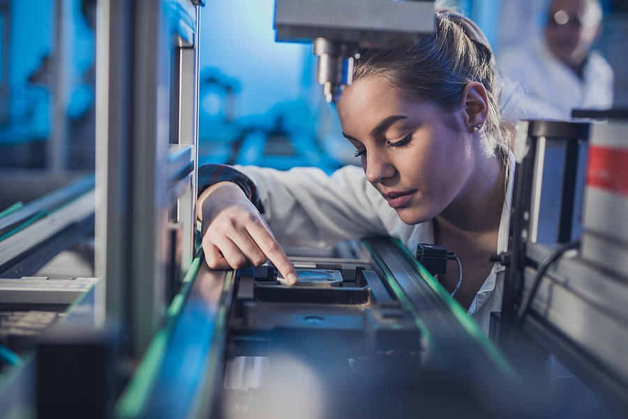 Female engineer examining machine part on a production line. #3 Photograph by Skynesher