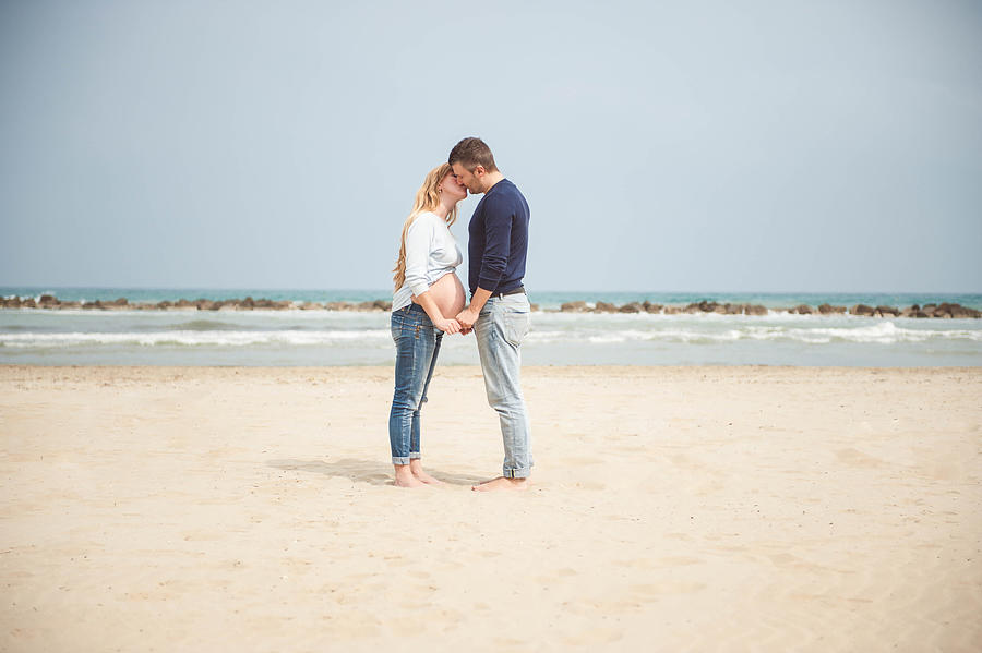 Pregnant couple kissing on the beach. Hand in hand. Casual clothes. #3 Photograph by © Samantha Carrirolo