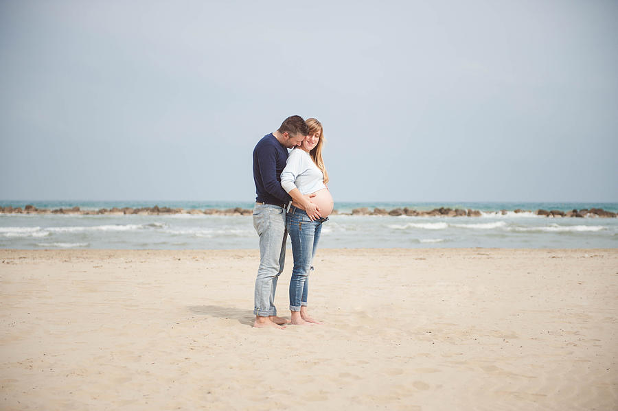 Pregnant couple on the beach. Hands on the belly. Embrace. Casual clothes. #3 Photograph by © Samantha Carrirolo