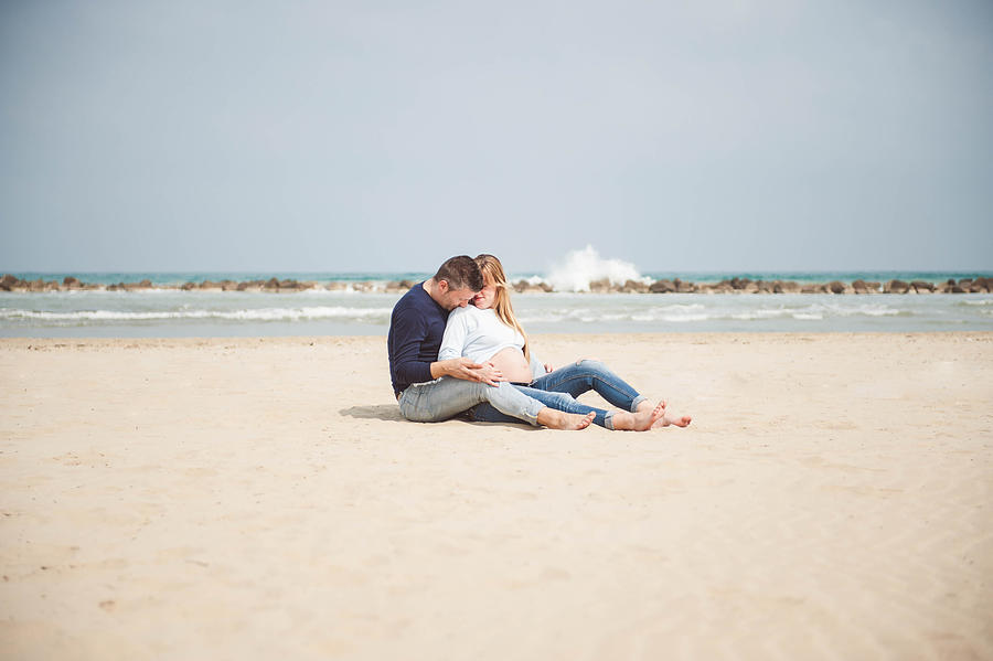 Pregnant couple sitting on the beach. Embrace. Casual clothes. #3 Photograph by © Samantha Carrirolo