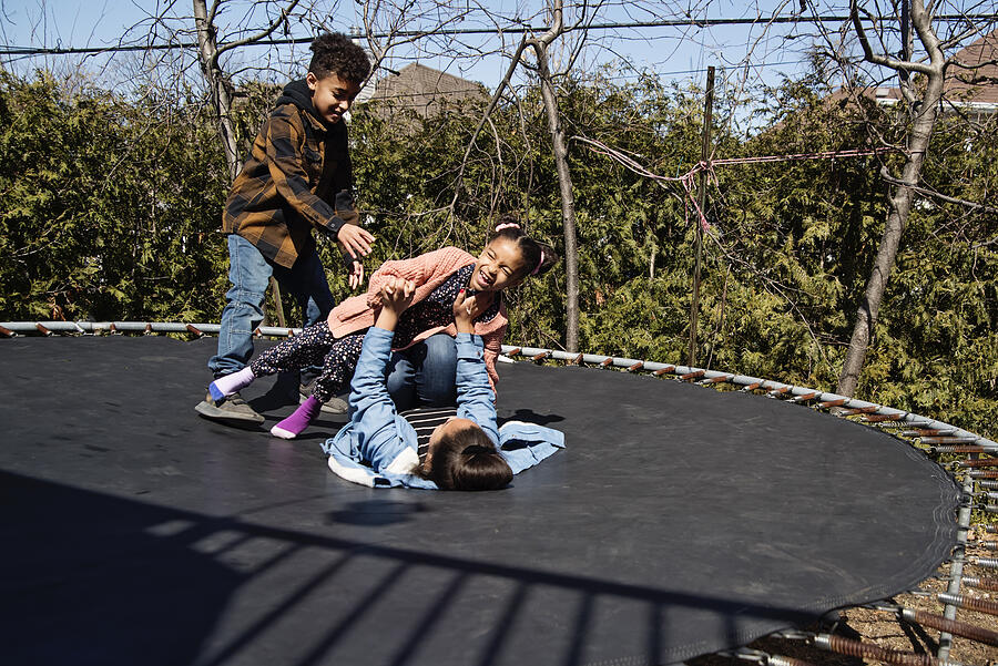 Siblings jumping on trampoline outdoors in springtime. #3 Photograph by Martinedoucet