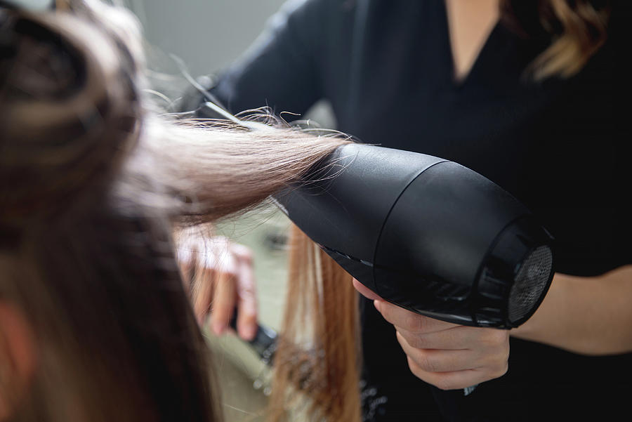 Close up of hairdressers hands drying long blond hair with blow dryer ...