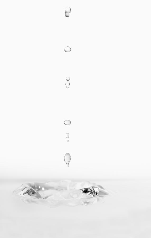 Group of drops on line suspended in the air, falling down on a water surface that forms figures and abstract forms, on a white background #4 Photograph by Jose A. Bernat Bacete