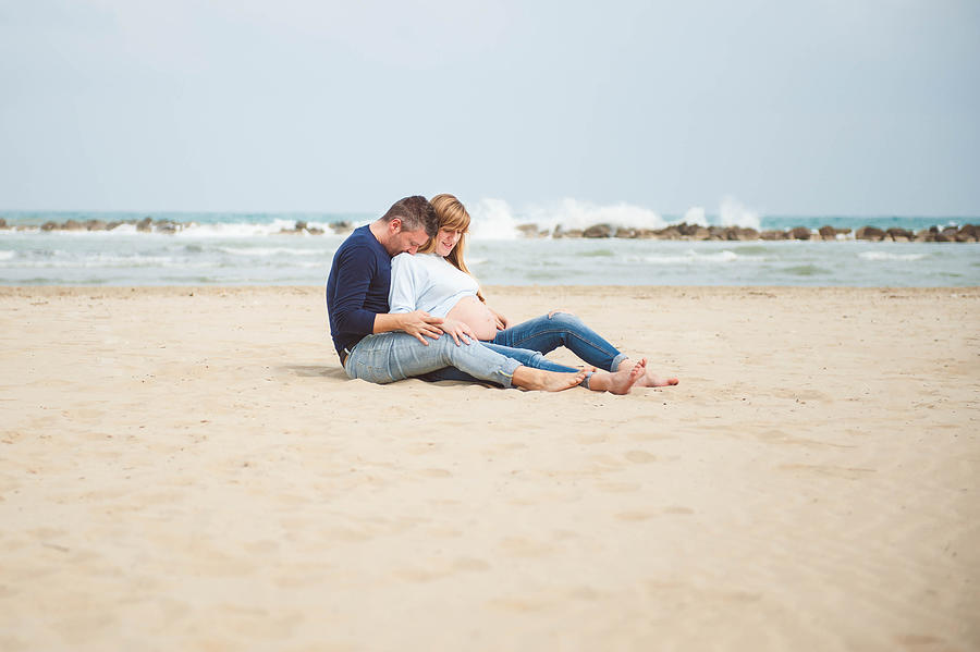 Pregnant couple sitting on the beach. Embrace. Casual clothes. #4 Photograph by © Samantha Carrirolo