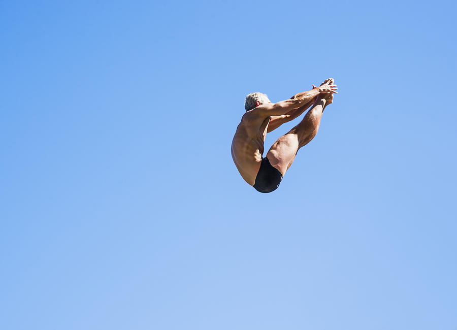 Athletic swimmer mid-air against blue sky #5 Photograph by Daniel Grill
