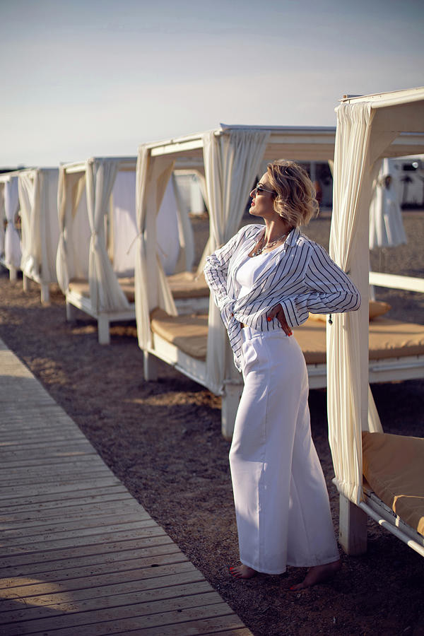 Woman In White Clothes And Sunglasses Is Standing On The Beach Near Wooden Photograph By Elena