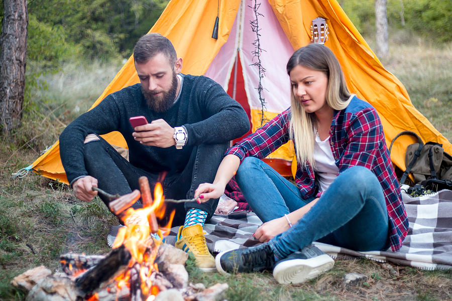 Beautiful couple, sitting, camping around the campfire. On the background with a tent The man flicks the fire with a stick. #8 Photograph by MajaMitrovic