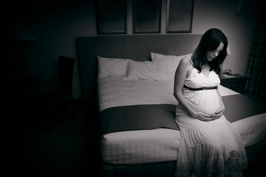 A black and white photo of a pregnant woman sat on the bed Photograph by Hidesy
