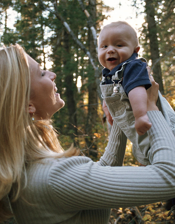 A Blonde Caucasian Mother Lovingly Holds Up Her Young Baby And Smiles Photograph by Photodisc