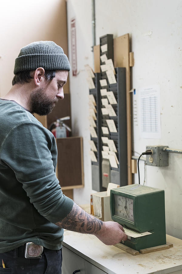 A Caucasian carpenter checking in with a time clock in a woodworking factory. Photograph by Mint Images