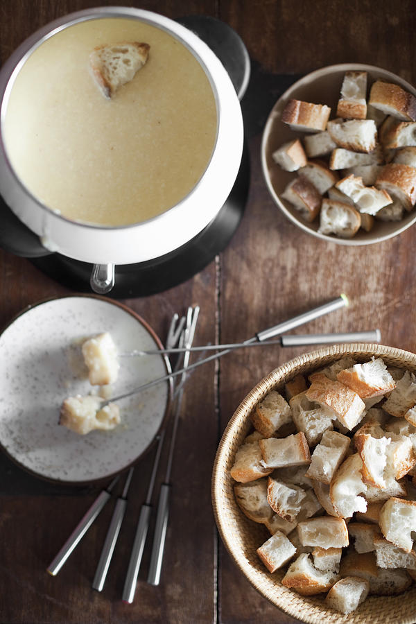 A cheese fondue on a table top. Cubed bread and long forks, for dipping bread into rich melted cheese mixture. Photograph by Mint Images - Britt Chudleigh