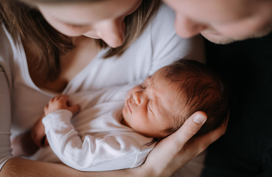 A close-up of a mother and father holding a newborn baby son at home. Photograph by Halfpoint Images