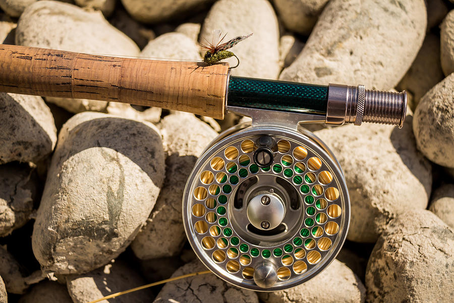 A close up of a trout fly rod, reel and line on rocks, with a