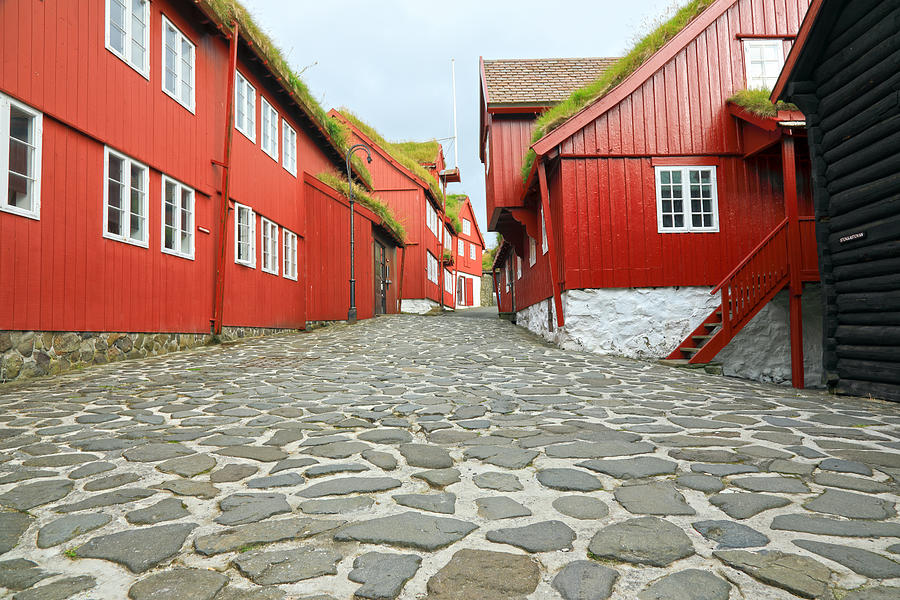 A cobblestone road through old wooden red buildings in the historic part of Tórshavn Photograph by Rainer Grosskopf