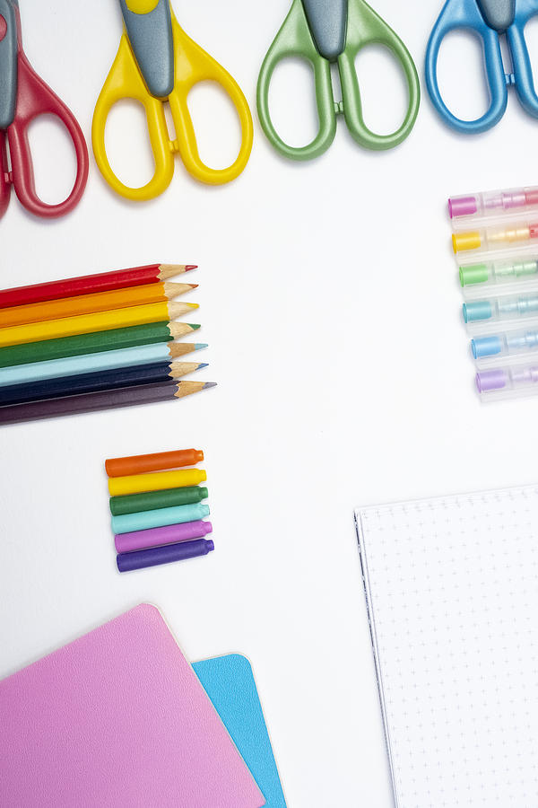A collection of rainbow coloured school supplies on a white background, portrait format Photograph by Catherine MacBride