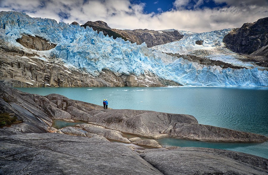 A couple of excursionist diminished by the scale of glacier Los Leones in Laguna Sn. Rafael NP Photograph by Fotografías Jorge León Cabello