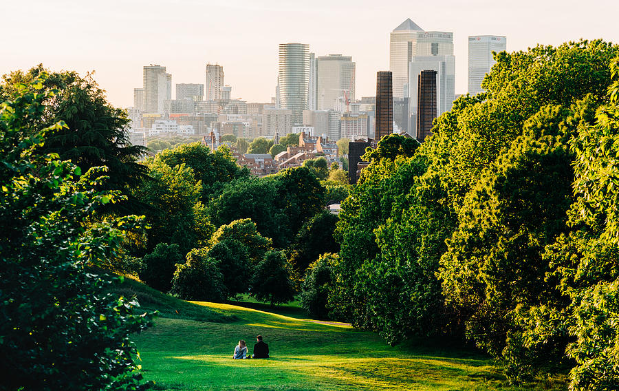 A couple sit in Greenwich Park, London looking the Canary Wharf skyline - stock photo Photograph by Karl Hendon
