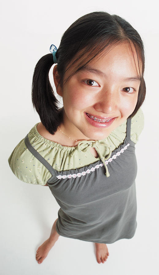 A Cute Asian Girl In Ponytails And Braces Wears A Gray Jumper And Stands Barefooted Looking Up Into The Camera Photograph by Photodisc