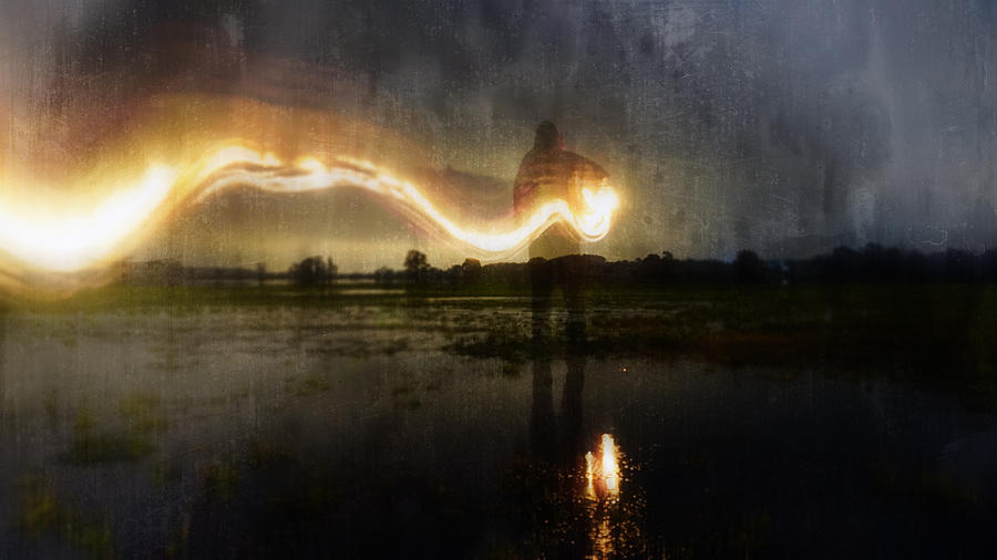 A deliberately blurred, abstract, out of focus, textured edit. Of a ghostly, eerie figure, standing in a flooded field, holding a glowing lamp with a flaming light trail behind. On a winters evening. Photograph by David Wall