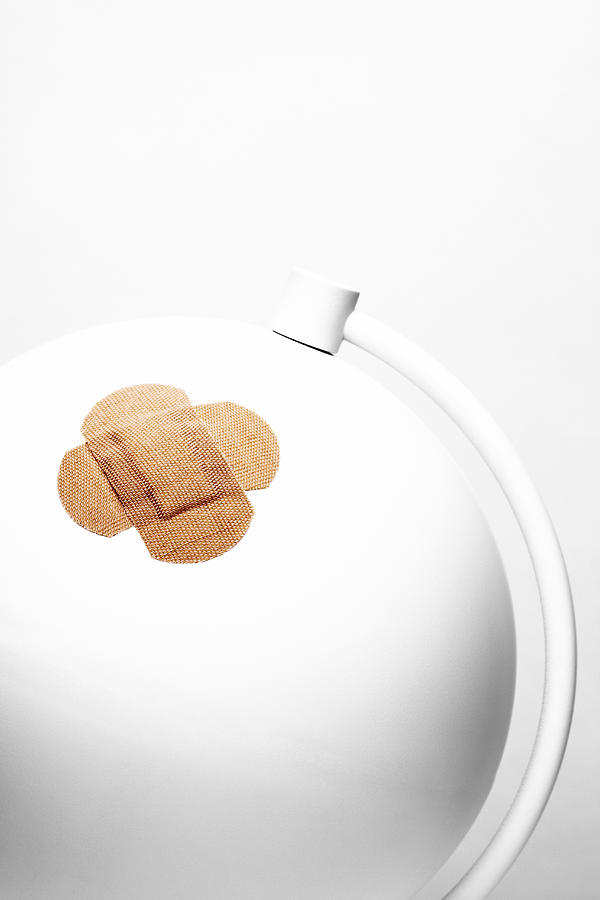 A desk globe has a sticking plaster stuck over a wound Photograph by Creative Crop