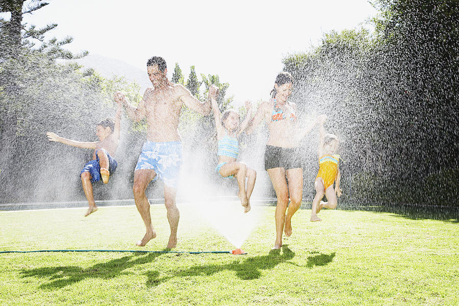 A family playing in a sprinkler Photograph by OJO Images