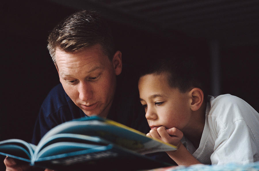 A Father Reads A Book To His Son Laying On The Bed Photograph by Photodisc