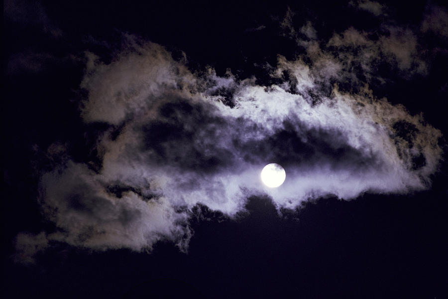 A Full Moon Peaks Out From Behind Darkness And Clouds At Night Photograph by Rubberball