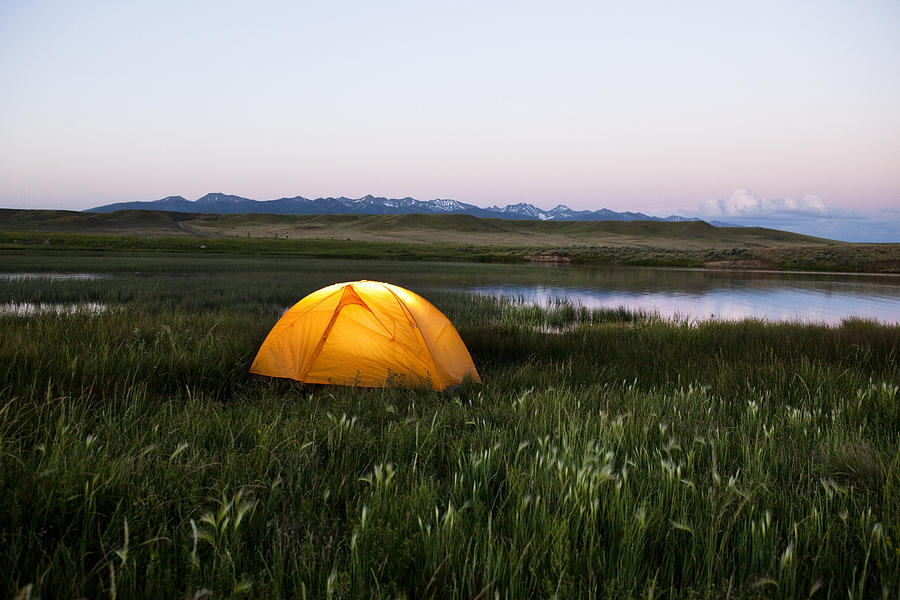 A glowing tent next to a lake at sunset in Montana. Photograph by Patrick Orton