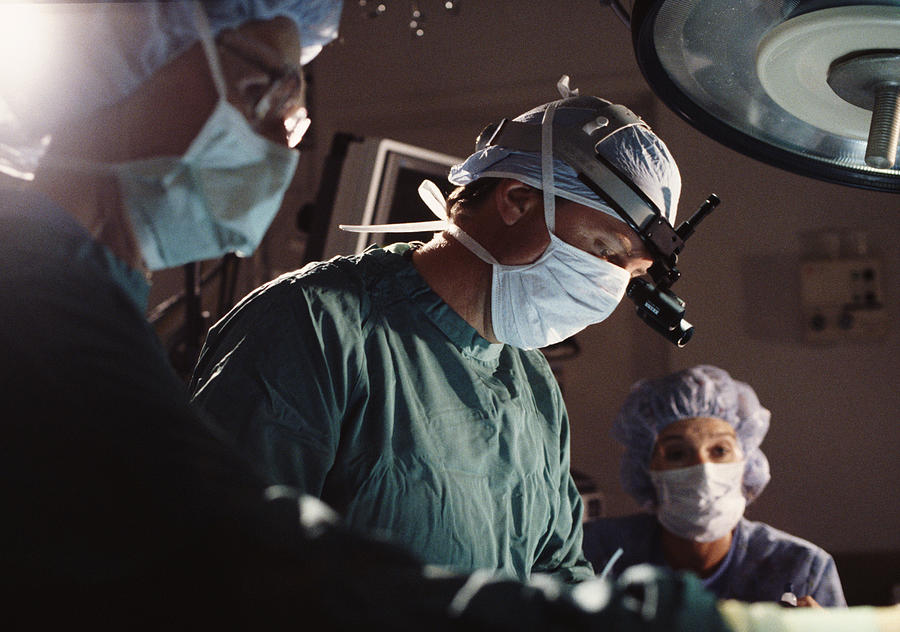 A Group Of Doctors And Nurses Perform Surgery In An Operating Room Photograph by Photodisc
